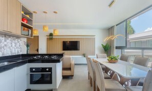 Una cocina moderna con una isla central, zona de comedor con sillas y un televisor montado en la pared.