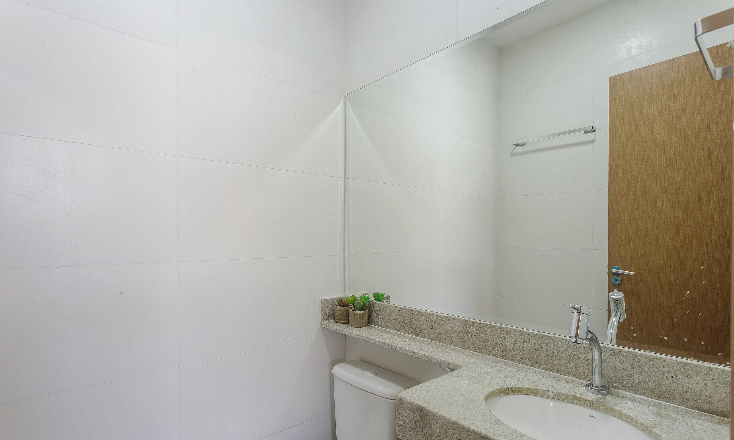 A bathroom with a white tiled wall, a wooden door, a sink with a mirror, and a shelf with potted plants.