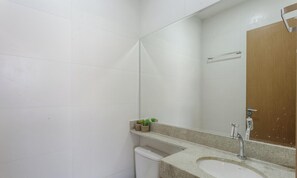 Un baño con pared de azulejos blancos, puerta de madera, lavamanos con espejo y repisa con plantas en macetas.
