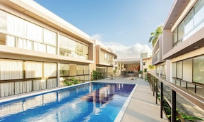 Un hotel moderno con piscina central, ventanas amplias y una zona de estar cubierta al aire libre.