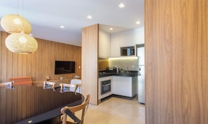 Una cocina moderna con paneles de madera, un comedor con una mesa y sillas oscuras, y un televisor montado en la pared.