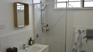 Un bagno con lavandino, specchio e doccia, tutto in bianco.