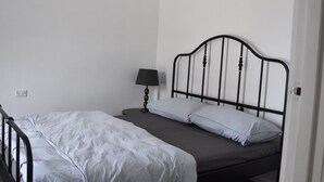 Un letto singolo con struttura in metallo, un comodino con lampada e una presa elettrica sulla parete.