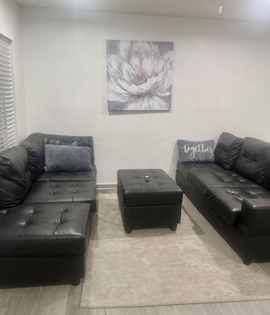 Ein Wohnzimmer mit zwei schwarzen Ledersofas, einem grauen Teppich und einem an der Wand hängenden abstrakten Gemälde.