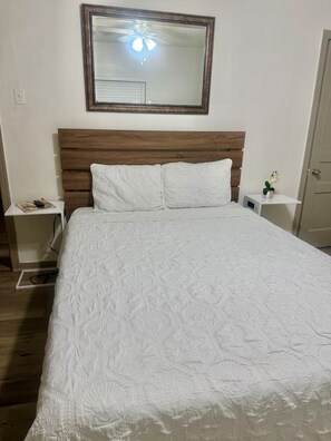 A bedroom with a wooden headboard, a white bedspread, and a nightstand with a lamp. - Great Location 3 Bedroom Cottage (Dallas)