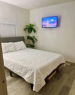 A bedroom with a bed, a television mounted on the wall, and a potted plant. - Great Location 3 Bedroom Cottage (Dallas)