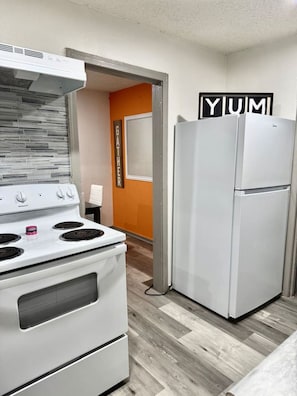 A kitchen with a white stove, a white refrigerator, and a wall with the word 'YUM' on it. - Great Location 3 Bedroom Cottage (Dallas)