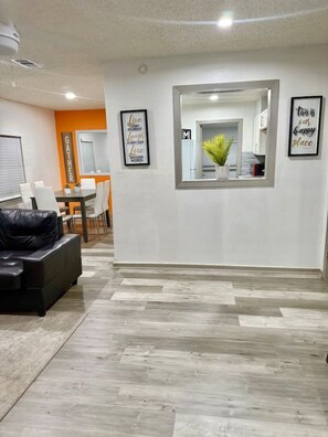 A modern living room with a black leather sofa, a dining area with a white table and chairs, and a kitchen area with a window and a potted plant. - Great Location 3 Bedroom Cottage (Dallas)