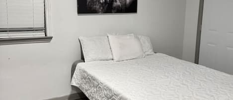 A bedroom with a bed, a window with blinds, a door, and a wall-mounted picture.