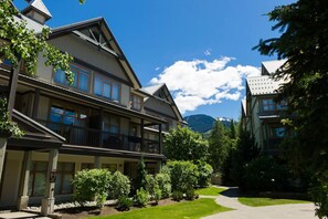 Un edificio di due piani con un balcone, immerso nel verde e con una montagna sullo sfondo.