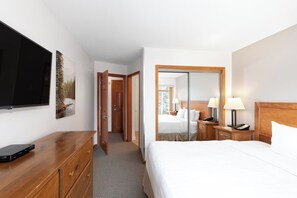Una camera d'albergo con un letto, comodini, una televisione, un comò in legno, uno specchio e una porta che conduce a un'altra stanza.