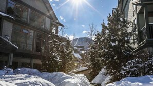 A snow-covered street with buildings on either side, a clear sky, and a mountain in the background. - Modern Whistler Stay | Full Kitchen & Fireplace for Cozy Nights (Squamish-Lillooet)