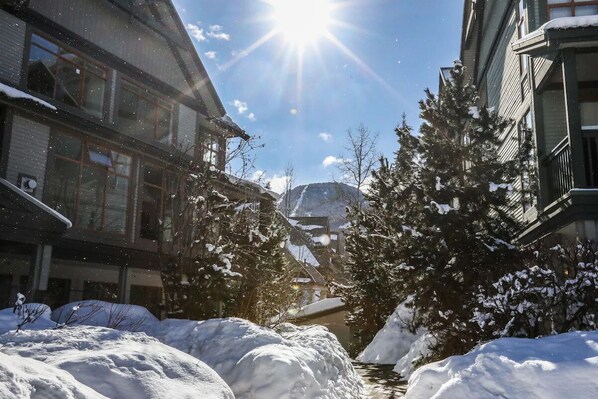 A snow-covered street with buildings on either side, a clear sky, and a mountain in the background.