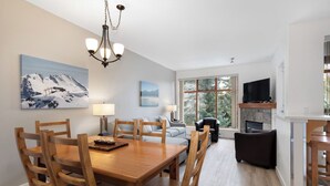 A dining area with a wooden table and chairs, a chandelier, and a painting of a mountain landscape. - Modern Whistler Stay | Full Kitchen & Fireplace for Cozy Nights (Squamish-Lillooet)