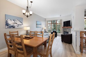 A dining area with a wooden table and chairs, a chandelier, and a painting of a mountain landscape.