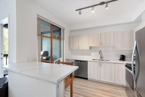 A modern kitchen with light wood cabinets, a white countertop, and stainless steel appliances.
