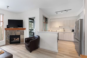 A modern kitchen with a built-in refrigerator, a flat-screen TV, and a stone fireplace.