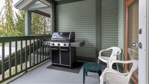 A covered porch with a grill, two plastic chairs, and a sliding glass door. - Modern Whistler Stay | Full Kitchen & Fireplace for Cozy Nights (Squamish-Lillooet)