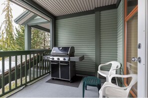 A covered porch with a grill, two plastic chairs, and a sliding glass door.