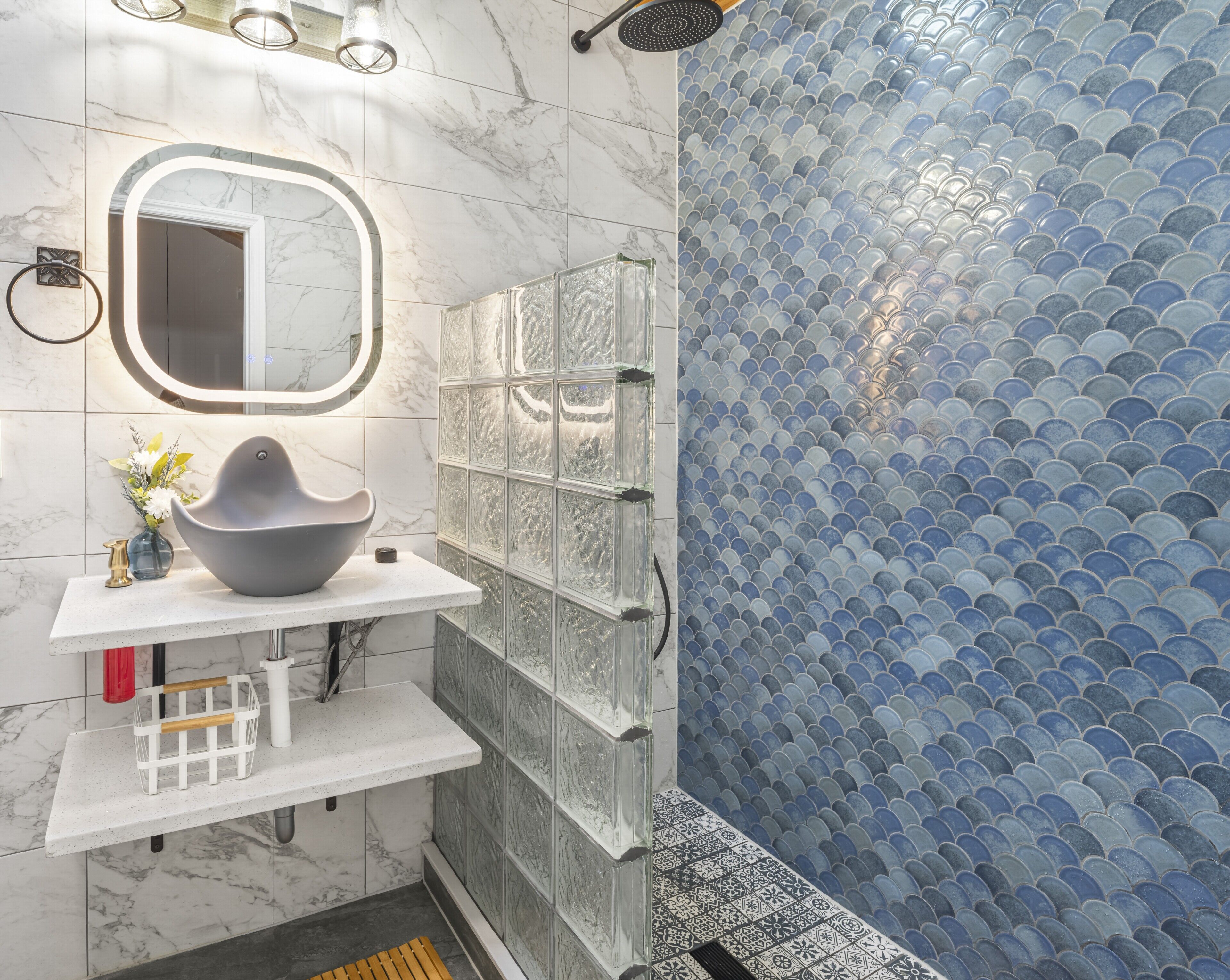 Une salle de bain avec un meuble-lavabo en marbre, une cabine de douche en verre et un mur recouvert de carreaux bleus.
