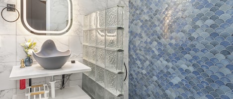 Un baño con tocador de mármol, cabina de ducha de vidrio y pared con azulejos azules.