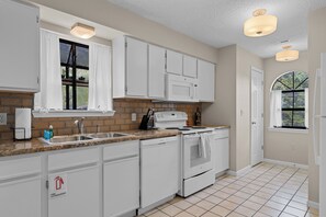 A kitchen with white cabinets, a stove, a sink, and a window with curtains. - 2BR/2BA Branson condo with king beds, pool, hot tub, and balcony. (Branson)