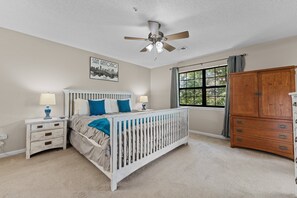 A bedroom with a white crib, a wooden dresser, a window with curtains, a ceiling fan, and a wall-mounted cityscape picture. - 2BR/2BA Branson condo with king beds, pool, hot tub, and balcony. (Branson)
