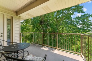 A covered outdoor area with a table and chairs, a metal railing, and a view of trees. - 2BR/2BA Branson condo with king beds, pool, hot tub, and balcony. (Branson)