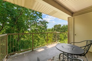 A balcony with a table and chairs, overlooking a lush green area. - 2BR/2BA Branson condo with king beds, pool, hot tub, and balcony. (Branson)