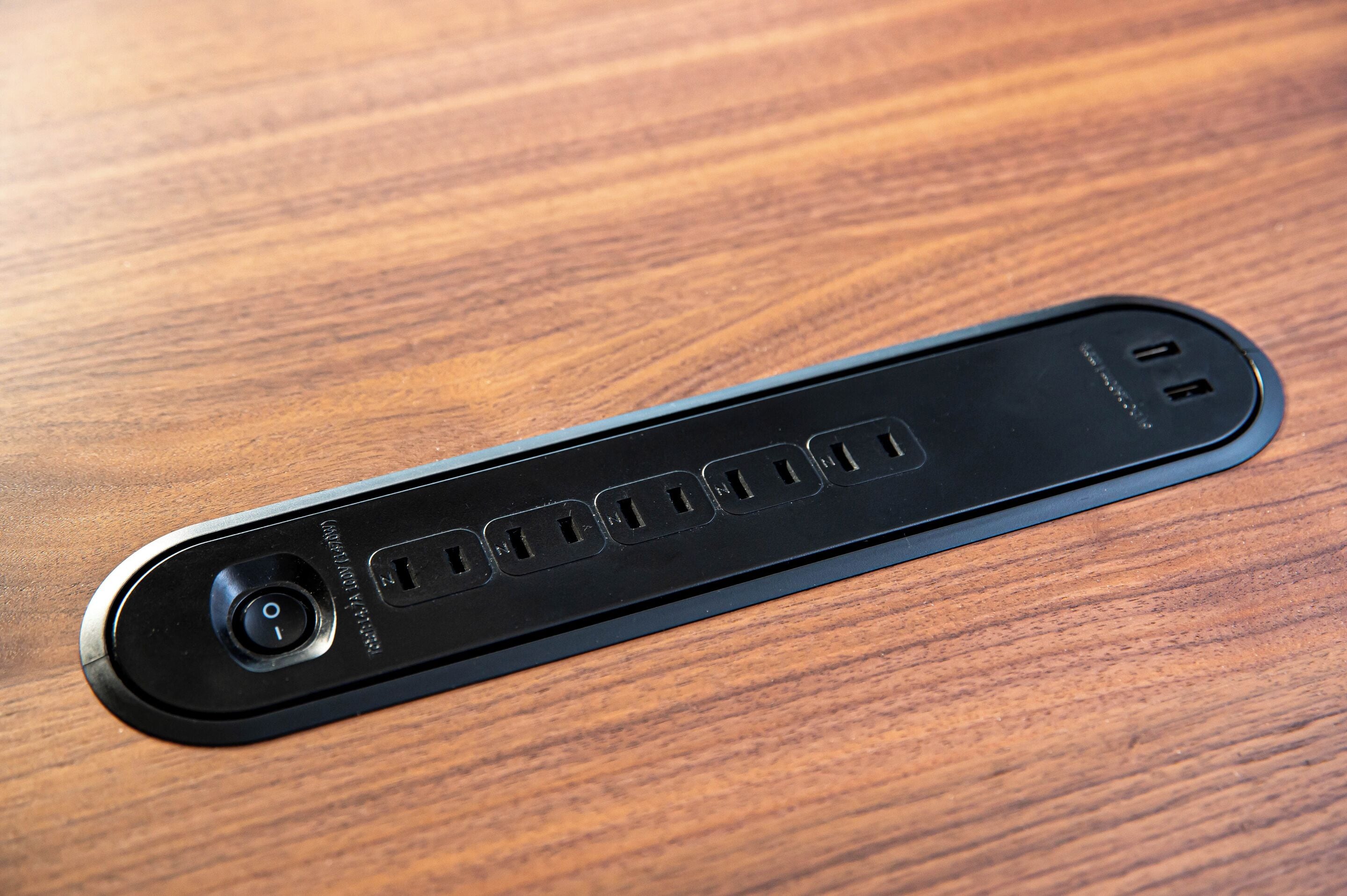 A black electronic device with a circular camera on the left and four rectangular ports on the right, placed on a wooden surface.