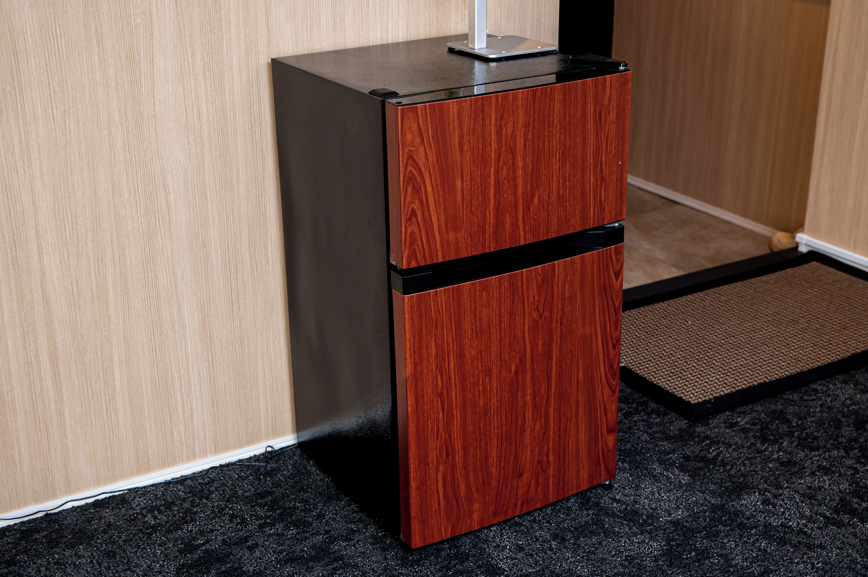 A small wooden cabinet with a black top, situated in a corner with a carpeted floor and a wooden wall.