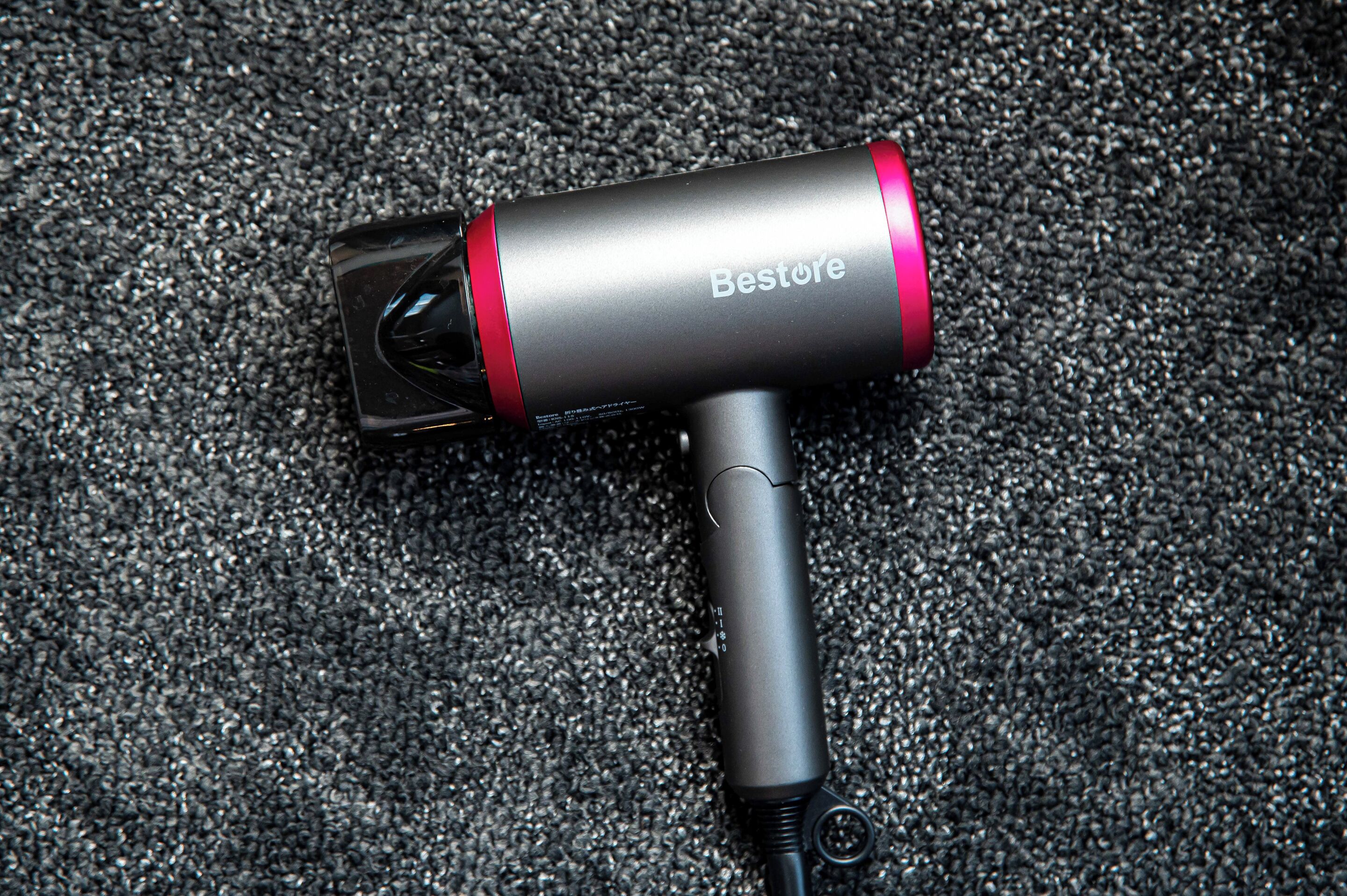 A black and red hairdryer with a cord, placed on a textured surface.