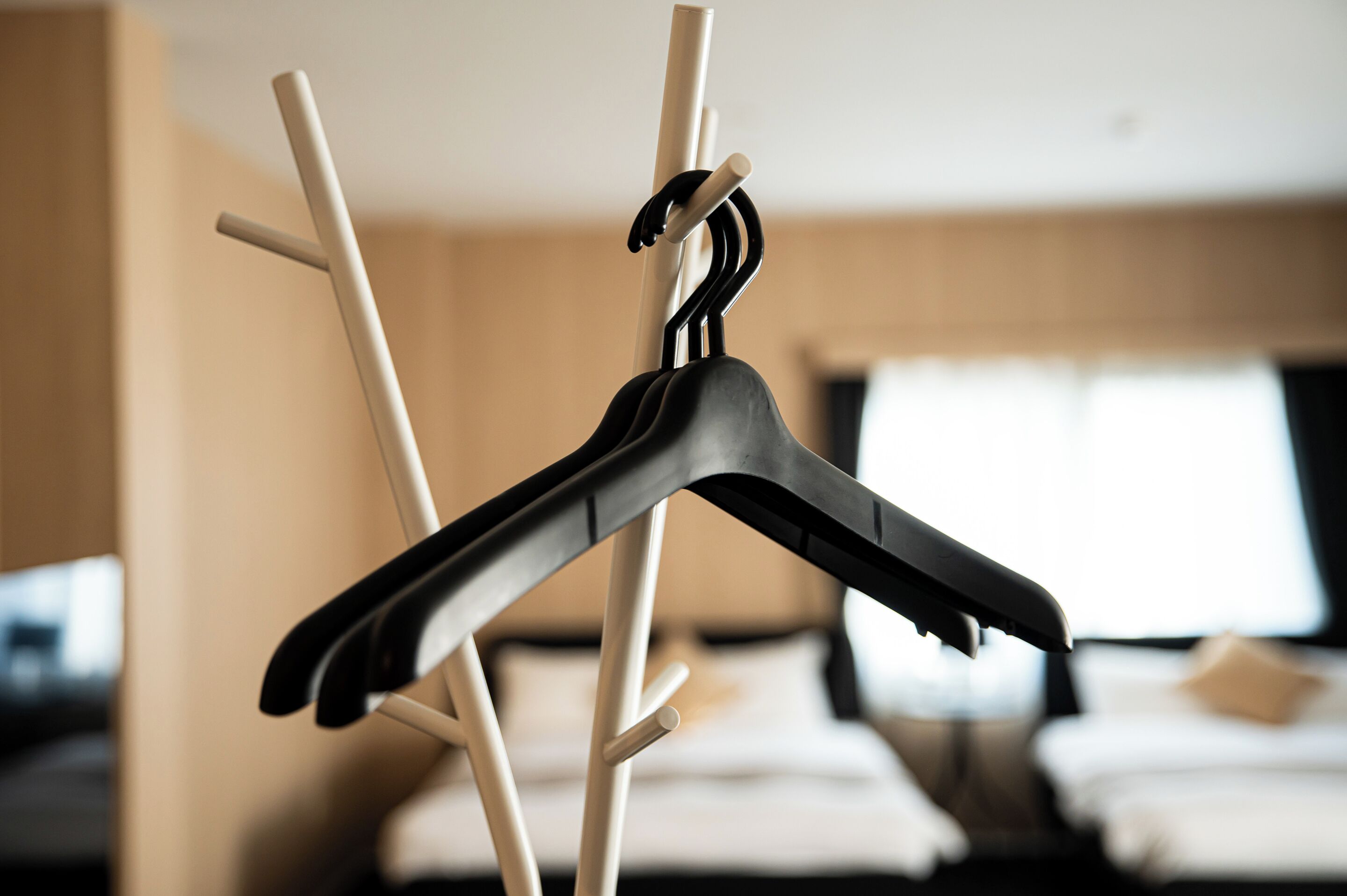 Quarto de hotel com uma cama, uma janela e um cabideiro com cabides.