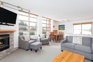 Ein modernes Wohnzimmer mit Kamin, grauen Sofas, einem Holztisch und einem Essbereich mit Tisch und Stühlen.