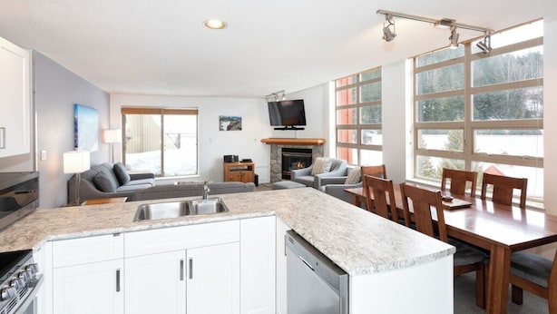 Een moderne keuken met een centraal eiland, een eethoek met houten stoelen, een open haard en een aan de muur bevestigde televisie.