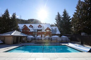Ein Schwimmbecken mit Rutsche, eine überdachte Poolterrasse und ein Gebäude mit schneebedecktem Dach.