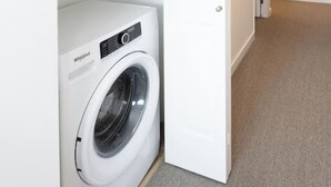 Een wasserette met een voorlader wasmachine en droger, een magnetron boven de droger, en een gang naar een andere kamer.