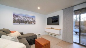 Ein modernes Wohnzimmer mit Sofa, Hocker, Wand-Fernseher und einem großen Landschaftsbild.