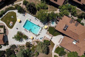 Ett flygbildsbild av ett bostadsområde med en rektangulär swimmingpool omgiven av en stenlagd uteplats.