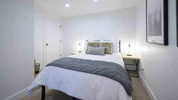 Ein Schlafzimmer mit einem Bett, Nachttischen, einer Tür und einem gerahmten Bild an der Wand.