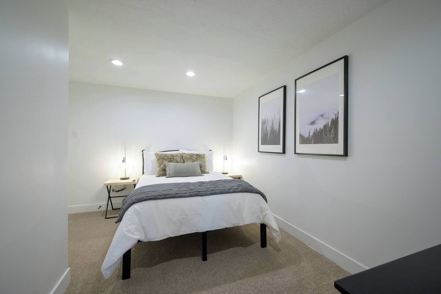 A bedroom with a bed, bedside tables, and two framed pictures on the wall.