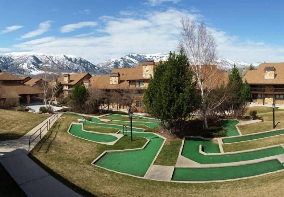 Un campo da golf con diverse zone verdi e montagne sullo sfondo.