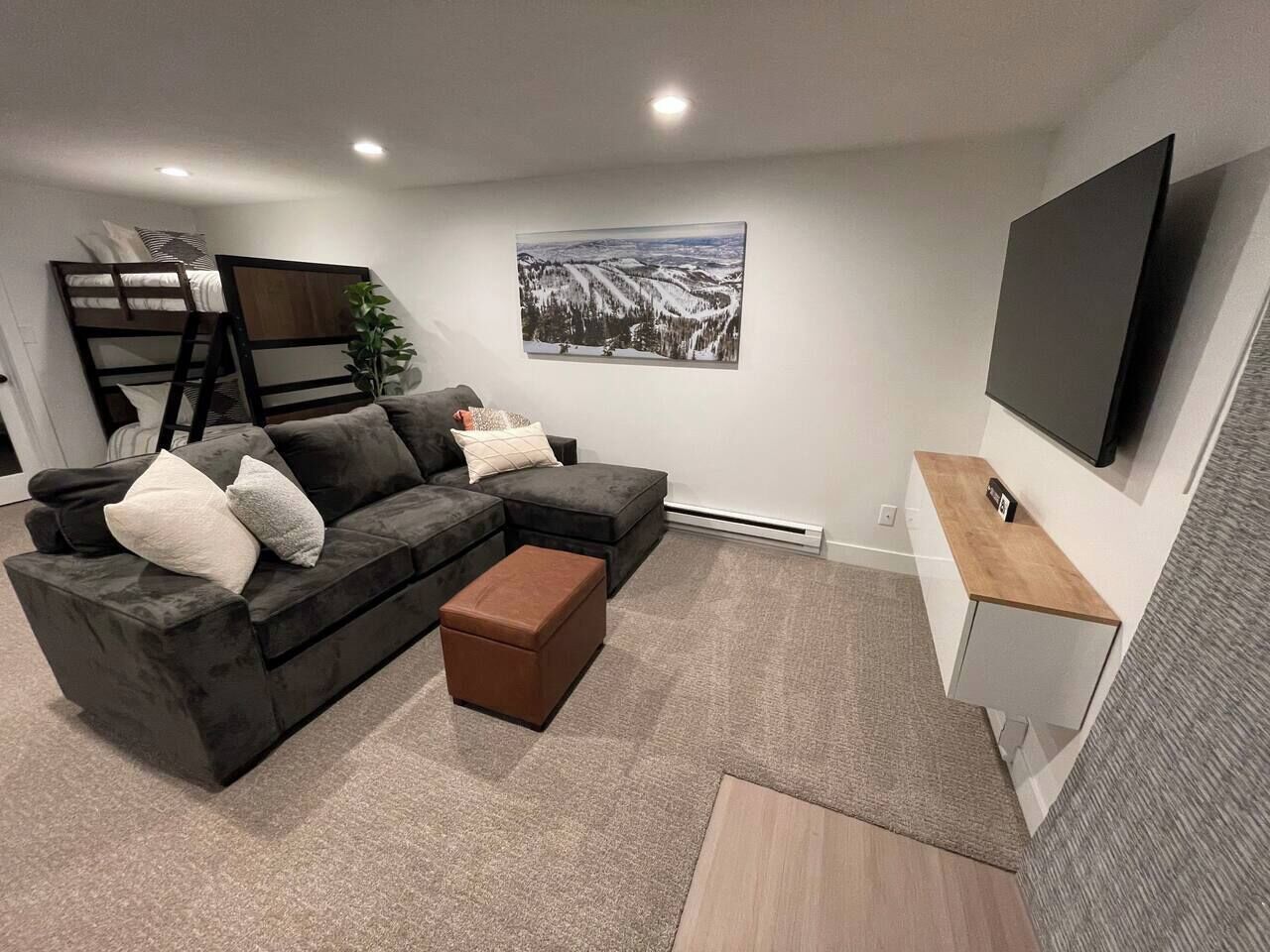 A modern living room with a sectional sofa, a coffee table, and a flat-screen TV mounted on the wall.