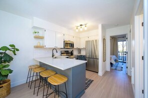 A modern kitchen with white cabinets, a central island with stools, stainless steel appliances, and a view to a balcony. - 2BR Mountain Condo | Community Pool & Hot Tub (Eden)