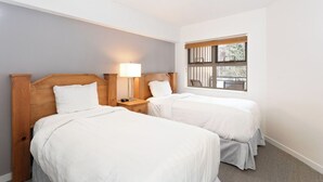 A hotel room with two single beds, a nightstand with a lamp, a window with a view of the outside, and light-colored walls. - Whistler Escape | Spacious Oasis w/ Mountain Views | Winter Outdoors (Whistler)