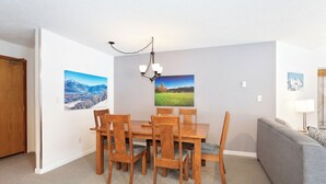 A dining area with a wooden table and chairs, a chandelier, and two wall-mounted pictures. - Whistler Escape | Spacious Oasis w/ Mountain Views | Winter Outdoors (Whistler)