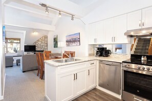 A modern kitchen with white cabinets, stainless steel appliances, and a dining area with a stone accent wall. - Whistler Creekside Stay | Modern Kitchen & Scenic Views | Near Gondola (Whistler)