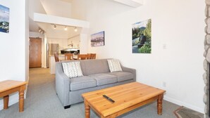 Ein modernes Wohnzimmer mit einem grauen Sofa, einem Holztisch und einem Essbereich im Hintergrund.