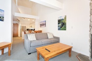 Ein modernes Wohnzimmer mit einem grauen Sofa, einem Holztisch und einem Essbereich im Hintergrund.