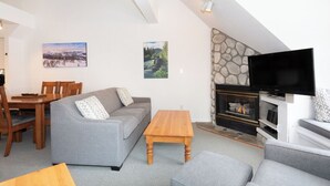 Ein Wohnzimmer mit Kamin, Fernseher, einer Couch, einem Holztisch und einer Essecke mit Stühlen und Tisch.
